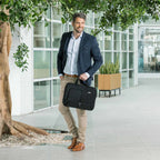 Man holding a black briefcase in an indoor setting with large windows and plants.
