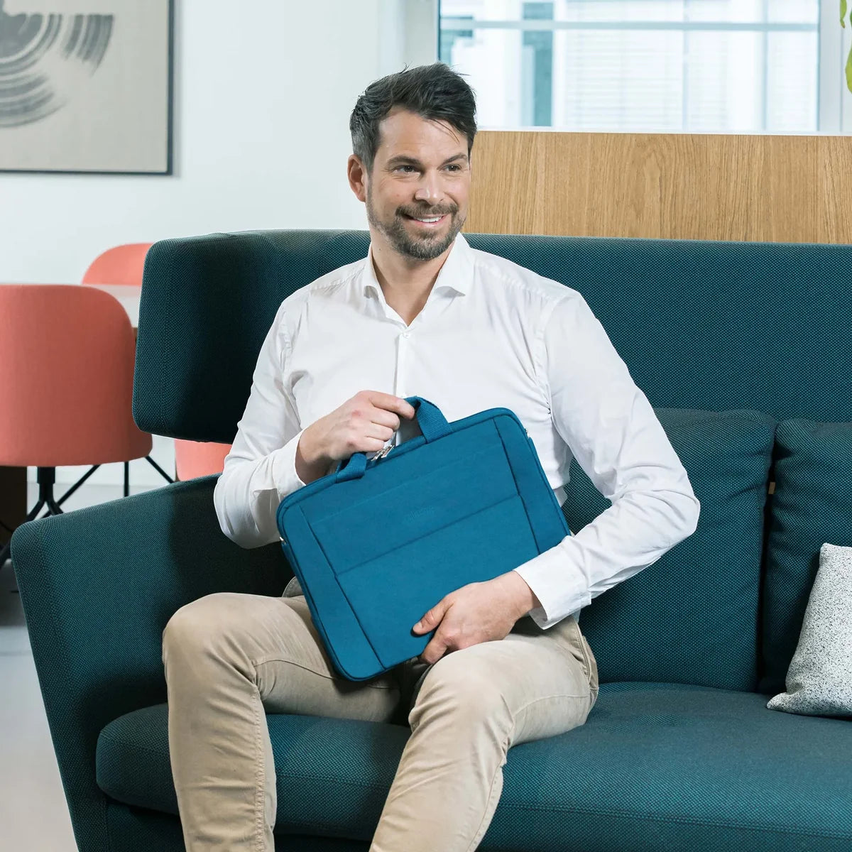 Man sitting on a blue couch holding a blue briefcase in an office setting.