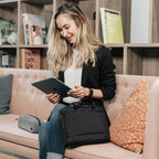Woman sitting on a couch using a tablet with a black bag beside her