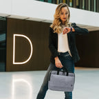 Woman holding a gray bag and looking at her watch in an indoor setting with a modern design.