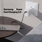 A white Picowatt wall charger plugged into a wall outlet, charging a silver laptop on a dark wooden table. The text 'Samsung -> Super Fast Charging 2.