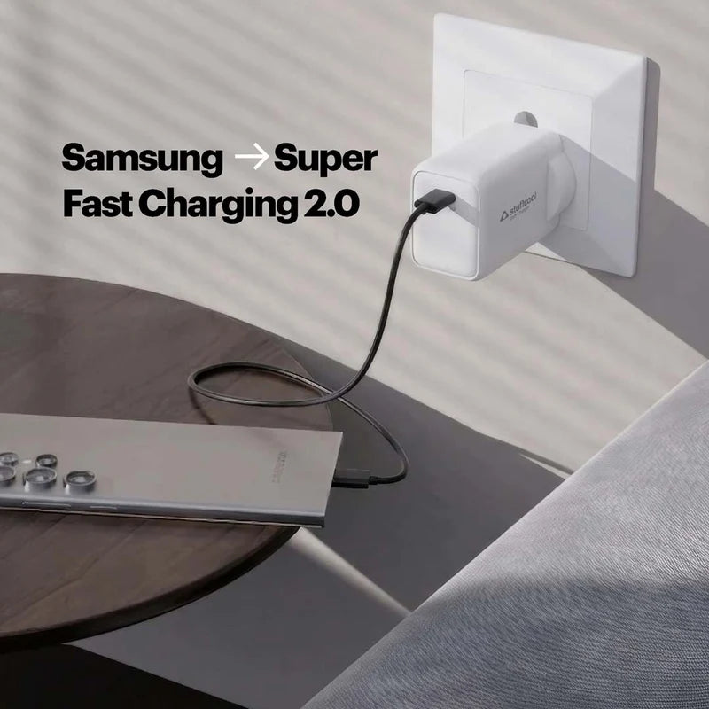 A white Picowatt wall charger plugged into a wall outlet, charging a silver laptop on a dark wooden table. The text 'Samsung -> Super Fast Charging 2.
