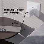 A white Pixelpower USB-C fast charger plugged into a wall outlet, charging a silver laptop on a dark wooden table. Text on the image reads 'Samsung -> Super Fast Charging 2.